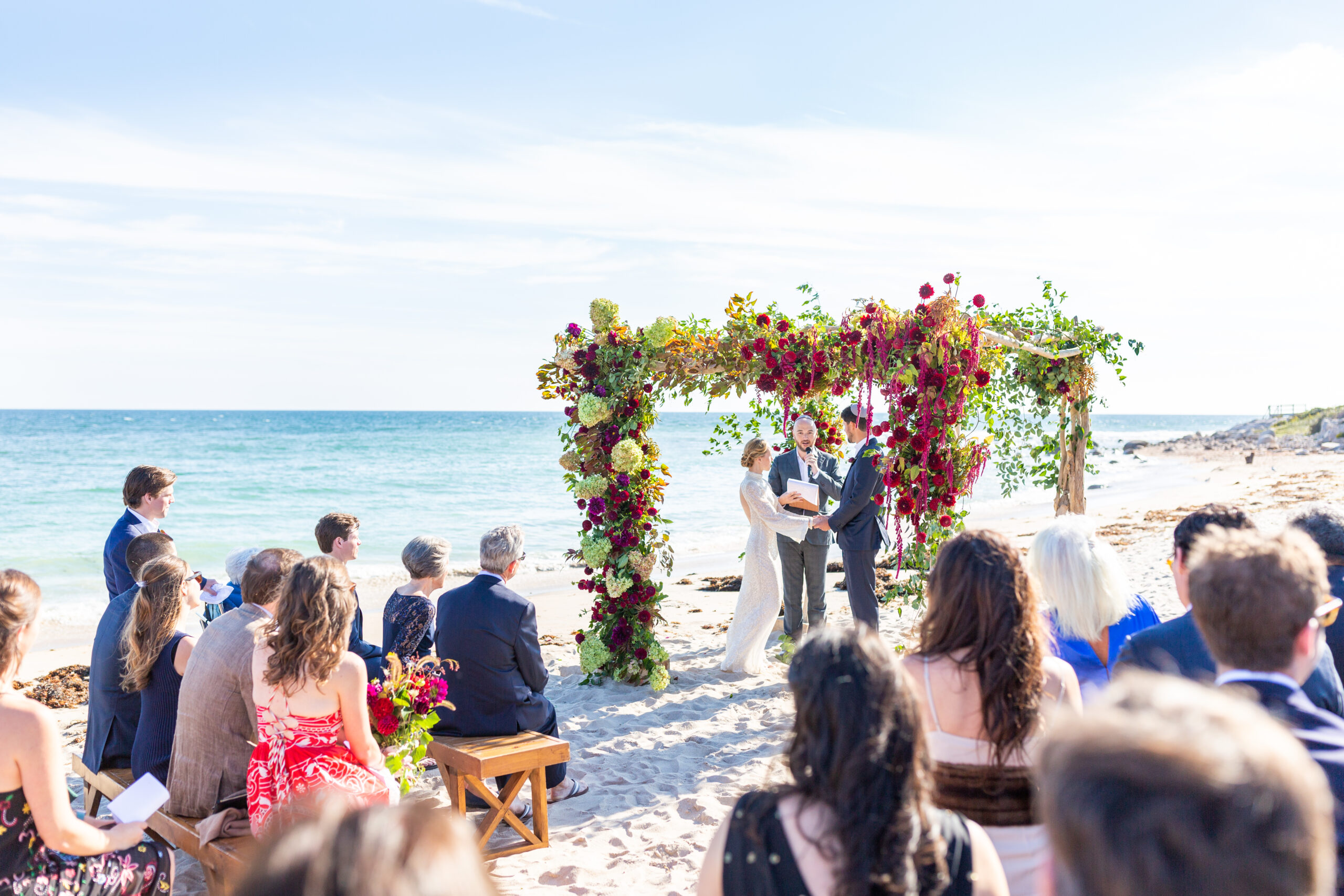 Bride and Groom stand under floral chuppah on the beach at their Weekapaug, RI Wedding
