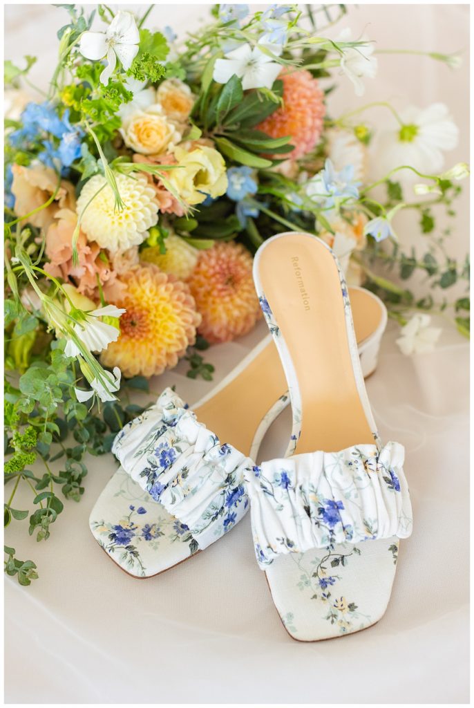 A bride's shoes displayed with colorful summer flowers in her bouquet. 