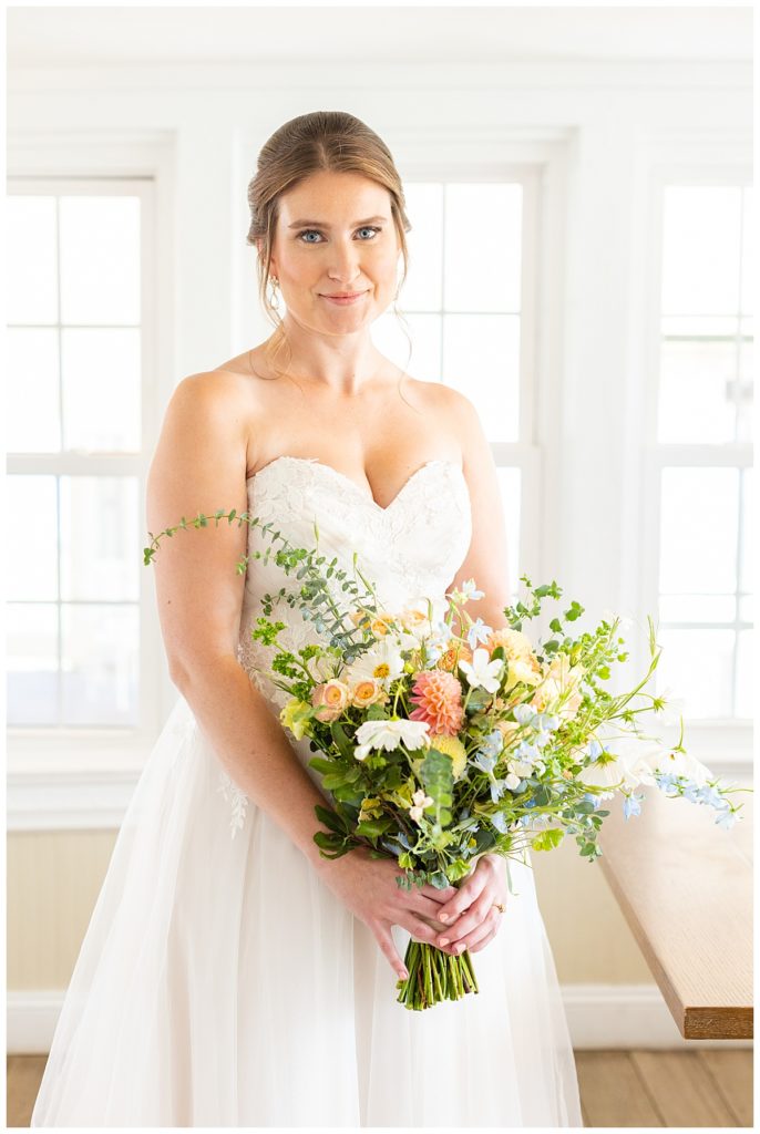 A bride holds her bouquet of colorful flowers, and smiles at the camera.