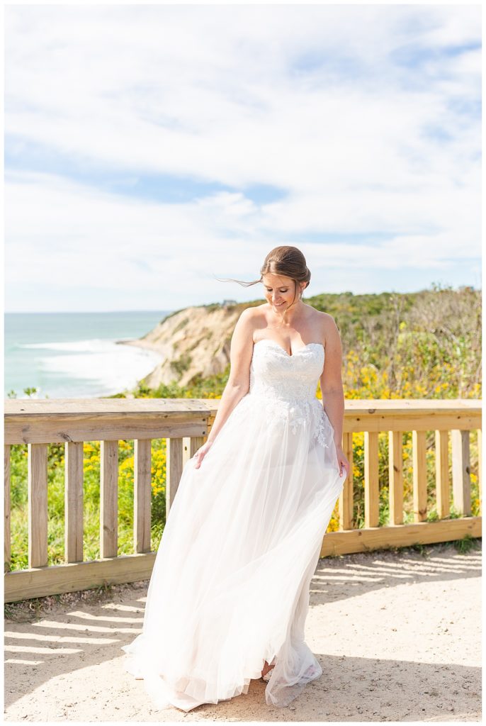 A portrait of a bride twirling in her dress in front of Mohegan Bluffs. 