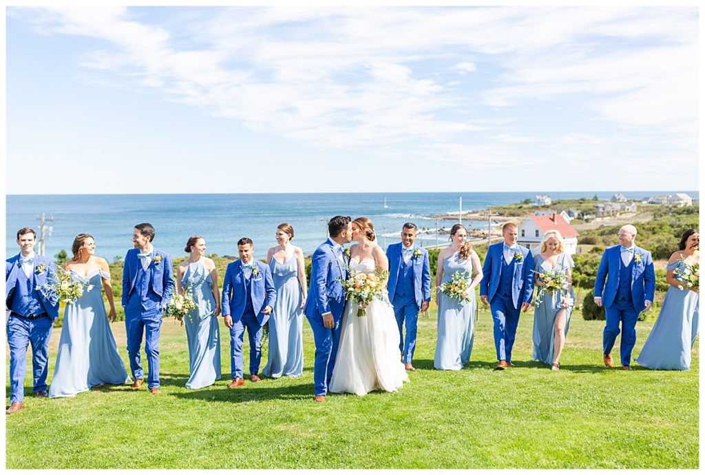 A bridal party walks on the lawn of the spring house with ocean views behind them. 