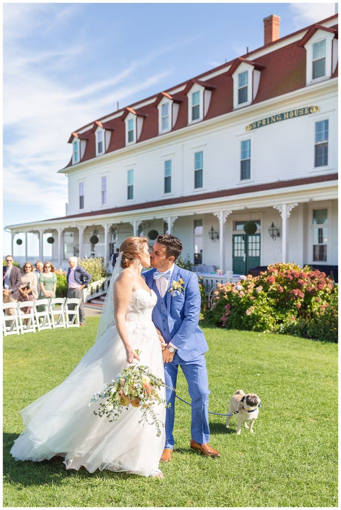 A bride and groom kiss after walking out of their wedding ceremony, with a view of the Spring house veranda behind them. 