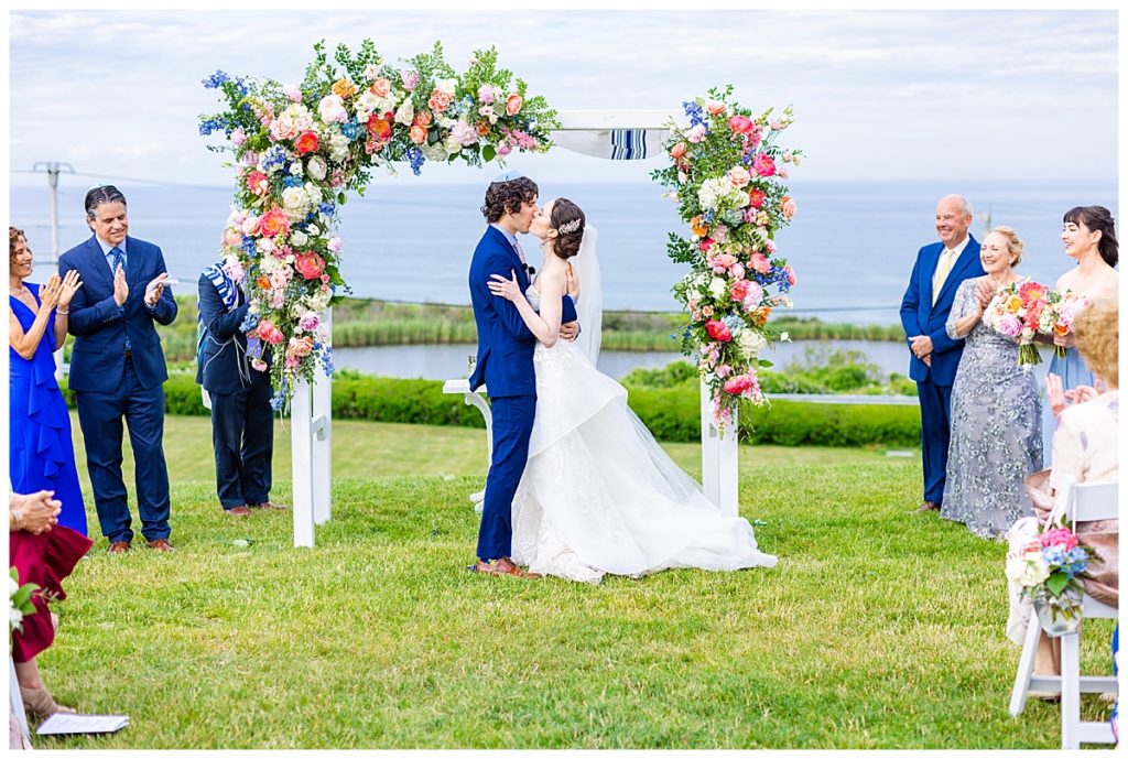 bride and groom kiss under ceremony chuppah overlooking Block Island coast