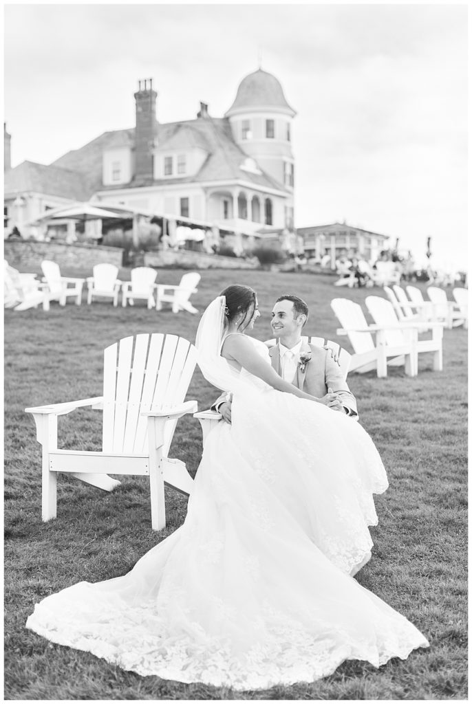 Bride and groom sit in an adirondack chair on the lawn at their Castle Hill Inn wedding. 