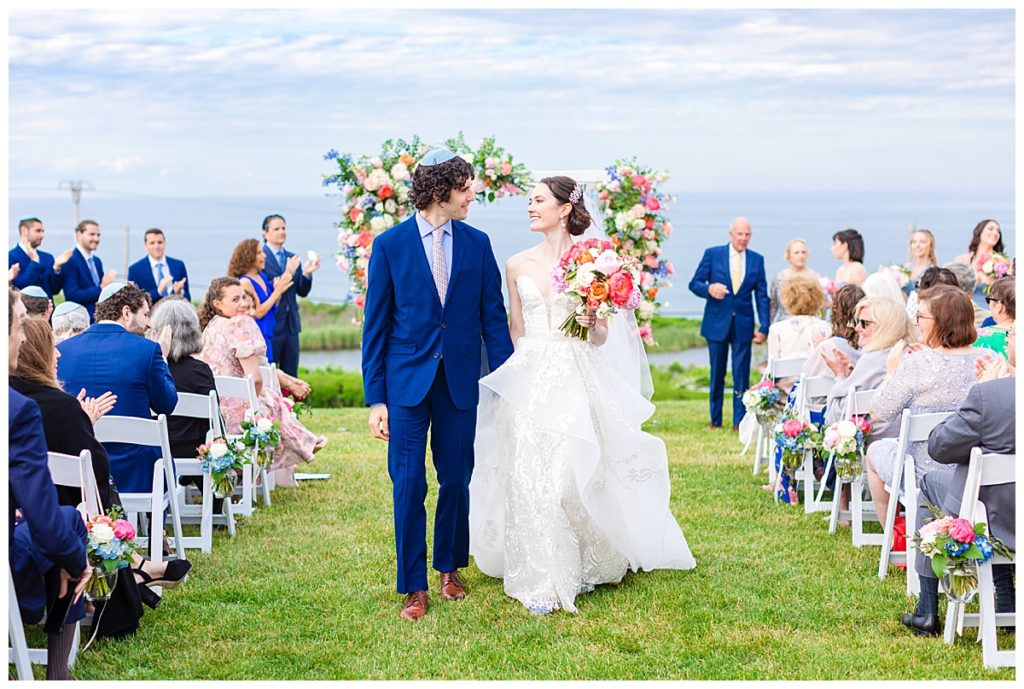 bride and groom recess down ceremony aisle amidst colorful floral arrangements