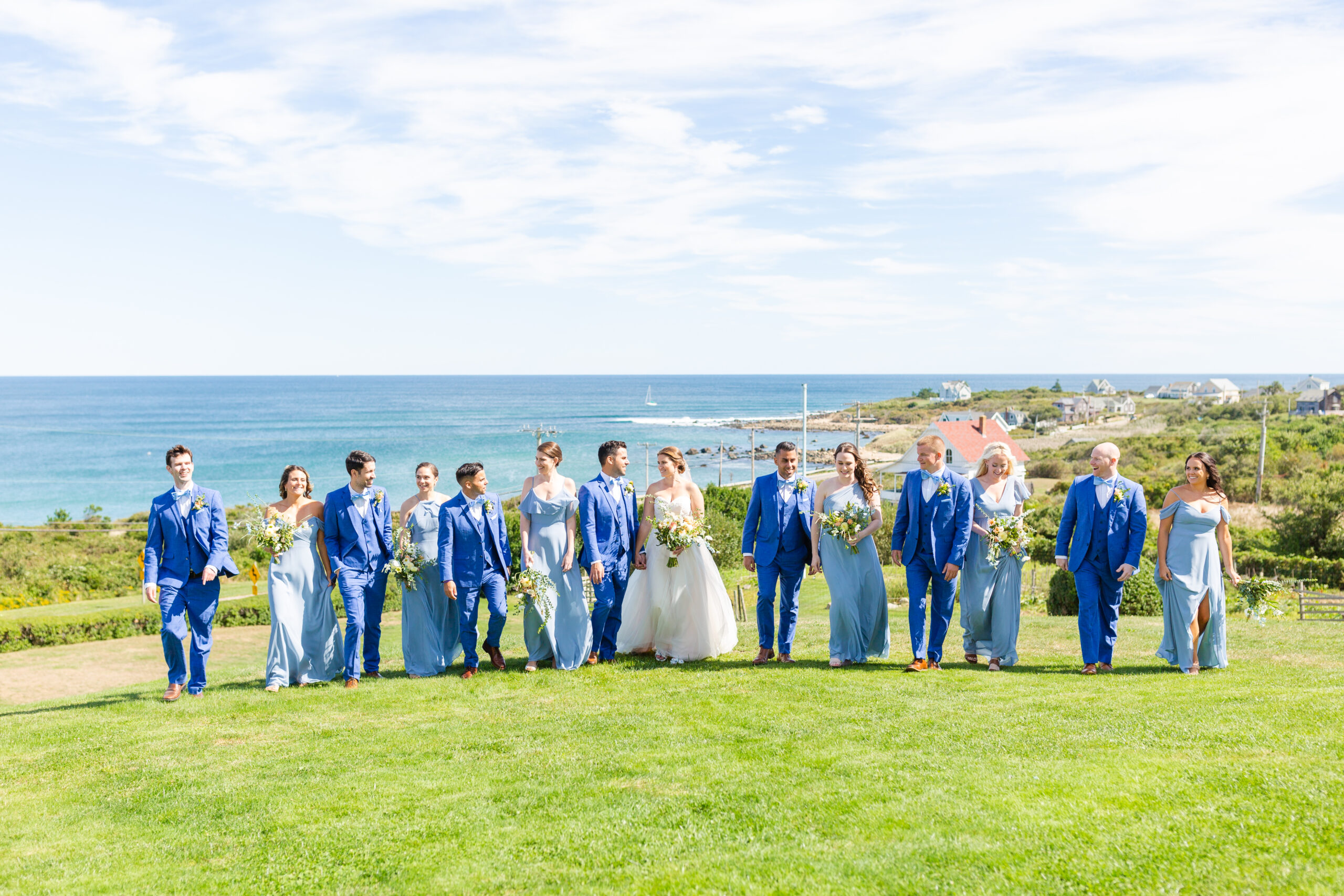Bridal party walks on lawn of Spring House during wedding with ocean view in the distance.