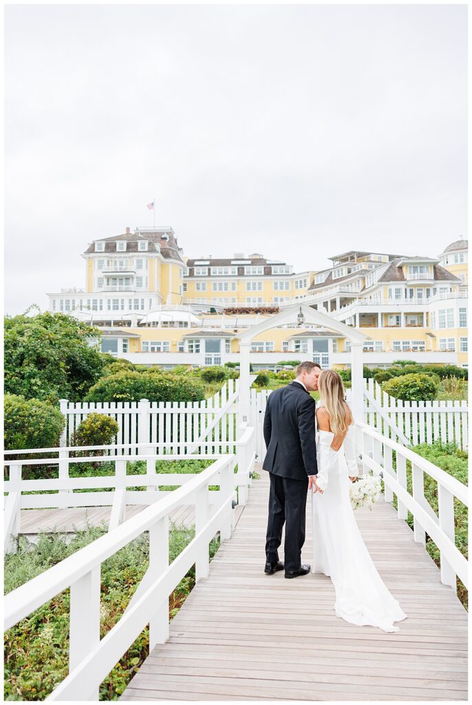 Bride and groom kiss on boardwalk at Ocean House with view of venue